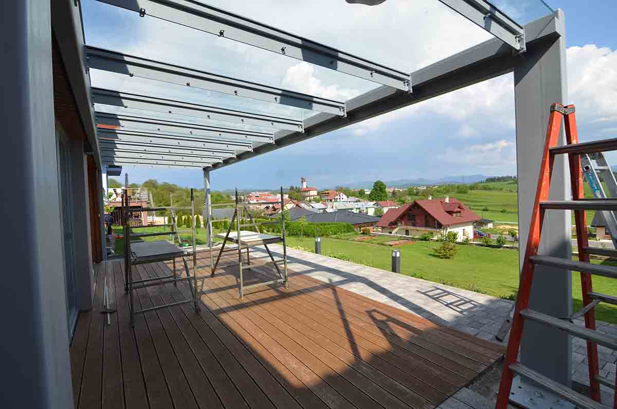 Montáž skleneného prístrešku s oceľovou konštrukciou a osádzanie skiel. Vrchné profily obsahujú prípravu na uchytenie drevených lamiel po celej dĺžke prístrešku. | DOMO GLASS